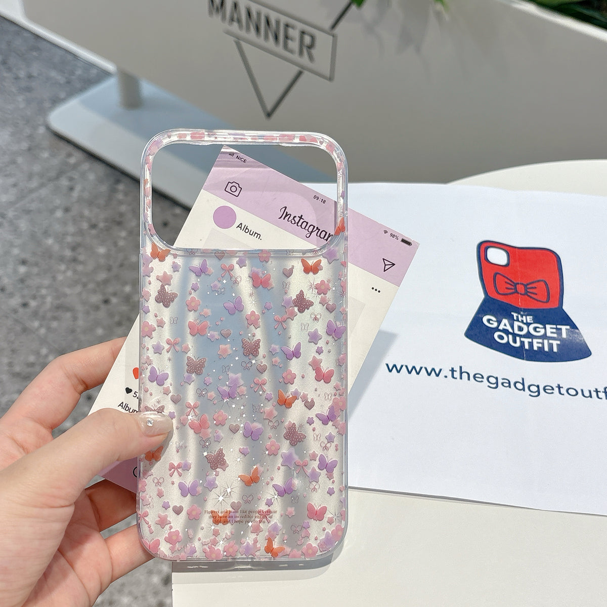 Phone case with butterfly pattern held by a hand, branded 'The Gadget Outfit' in the background.