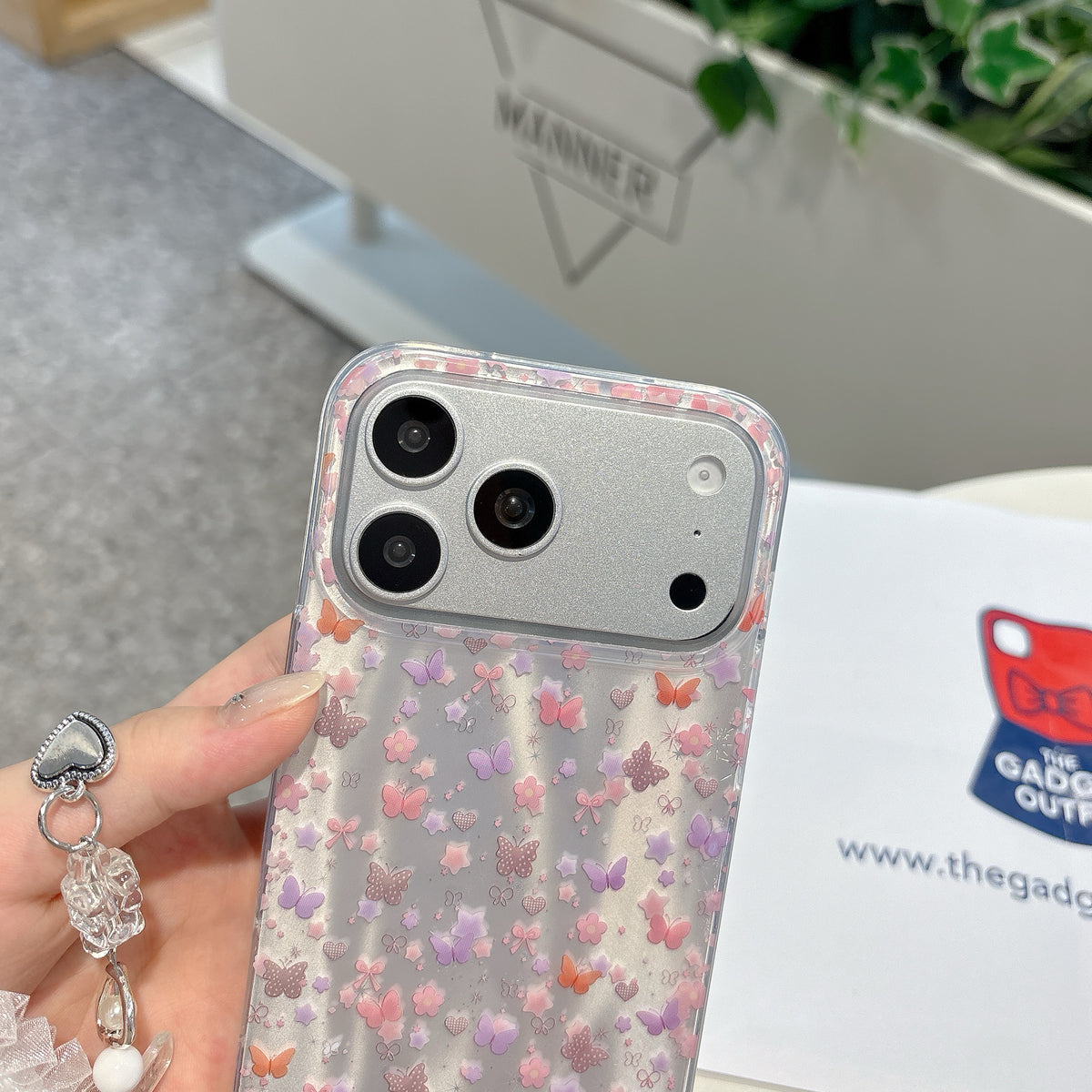 Phone case with butterfly pattern held by a hand, blurred background