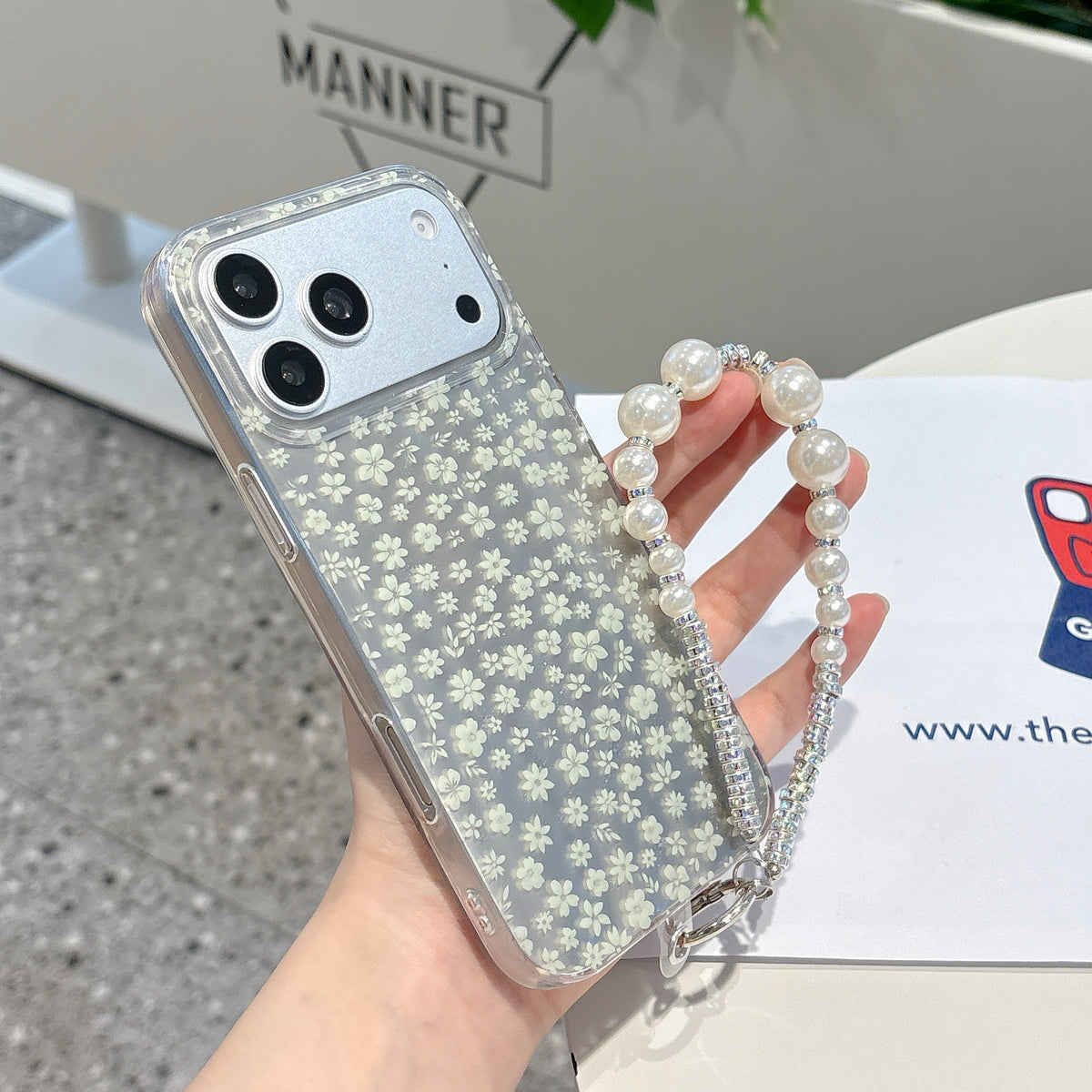 Phone case with floral pattern and pearl strap held by a hand, with a blurred background.
